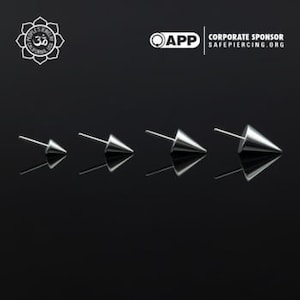 Puede incluir: Cuatro tachuelas de nariz cónicas de plata de diferentes tamaños, mostradas sobre una superficie negra reflectante.