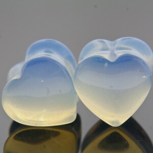 May include: Two heart-shaped plugs made of opalite, a translucent blue and white stone. The plugs are smooth and polished.