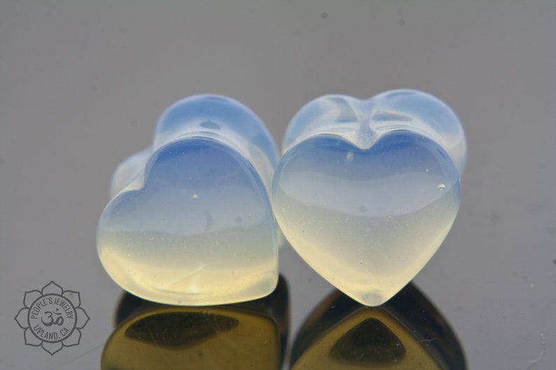 May include: Two heart-shaped plugs made of opalite, a translucent blue and white stone. The plugs are smooth and polished.