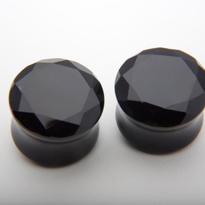 May include: Pair of black faceted glass ear gauges. The gauges are round and have a shiny finish.