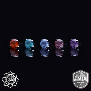 May include: Five different colored gemstone earrings, each with a silver setting. The gemstones are orange, teal, light blue, pink, and purple.