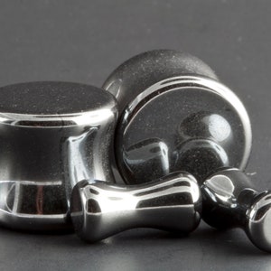 May include: Three black hematite ear gauges, one pair of plugs and one single flare, with a polished finish.