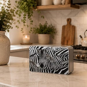 May include: A rectangular metal storage tin featuring a high-contrast black and white photographic print of a zebra. The design covers the front panel, showcasing the animal's distinct striped pattern and face in a clear, detailed graphic display.