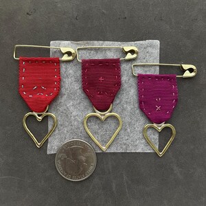 punk heart medals in poppy orange garnet red and raspberry grosgrain ribbon and hand wrought brass hearts by camille hempel design