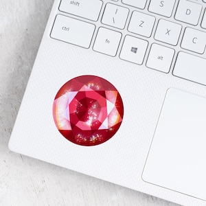 May include: A red gemstone sticker on a white laptop keyboard. The sticker is a close-up of a red gemstone with a faceted design.