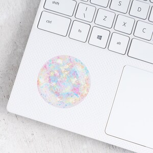 May include: A white laptop computer with a rainbow glitter sticker on the lid. The sticker is a circle with a holographic finish.