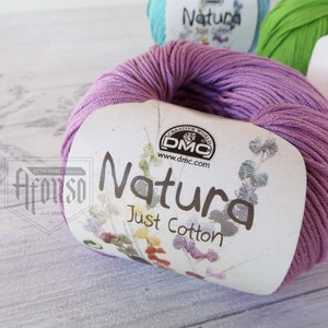 May include: A skein of purple cotton yarn labeled "Natura Just Cotton" by DMC. The yarn is wound around a white label with a floral design.