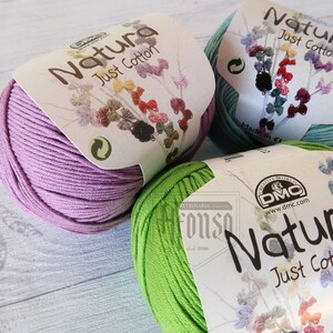 May include: Three skeins of Natura Just Cotton yarn in shades of lavender, green, and light blue. Each skein has a white label with the brand name and the words "Just Cotton".