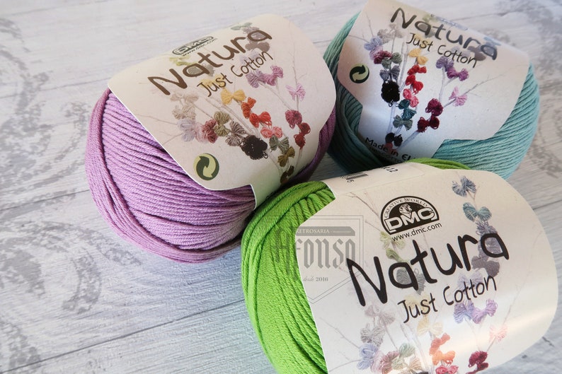 May include: Three skeins of Natura Just Cotton yarn in shades of lavender, green, and light blue. Each skein has a white label with the brand name and the words "Just Cotton".