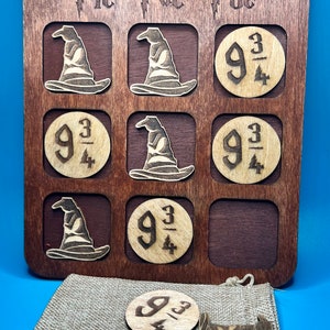 May include: A wooden tic-tac-toe game with a Harry Potter theme. The game board is brown and features a wizard hat and the number "9 3/4" as game pieces. The game pieces are stored in a brown burlap bag.