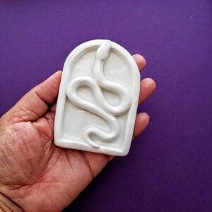 May include: White ceramic dish with a raised snake design. The snake is curled up in a circle and has a smooth, glossy finish.