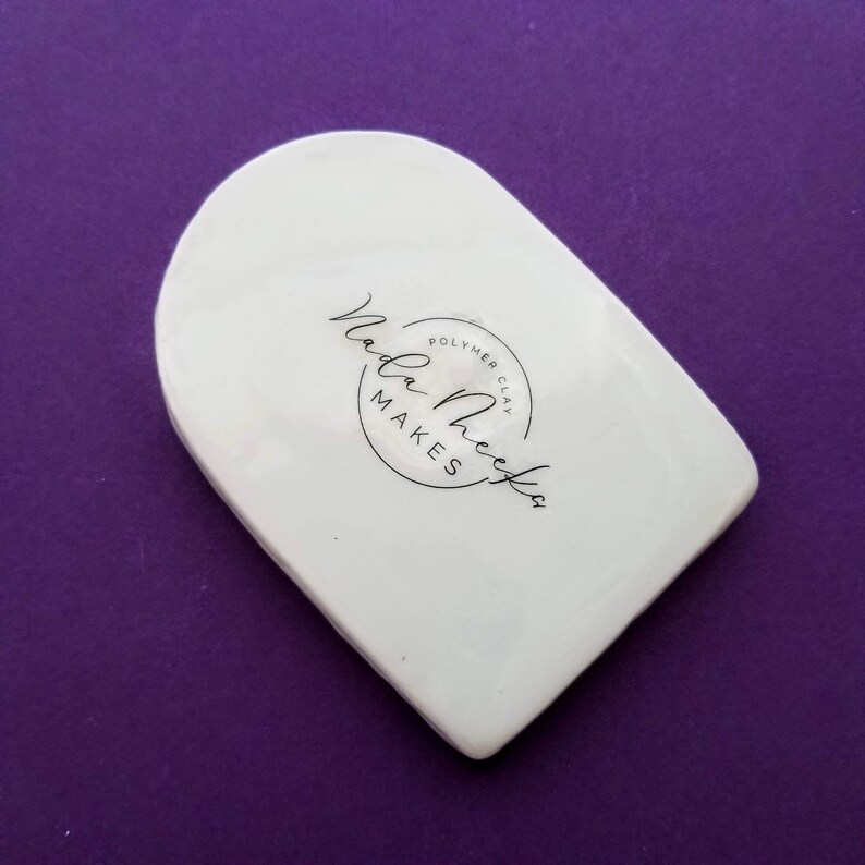 May include: White ceramic arch-shaped mold with the text "Nala Makes Polymer Clay" in a black circle.