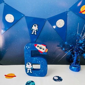 Letras o números decorados con astronautas del espacio exterior para fiestas de cumpleaños con temática espacial.