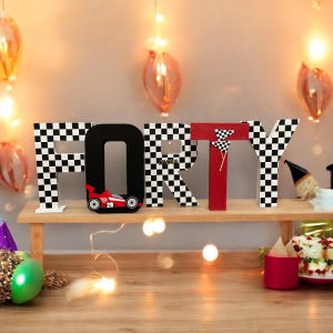 May include: Black and white chequered wooden letters spelling out "FORTY" with a red racing car on the "O". The letters are on a wooden shelf.