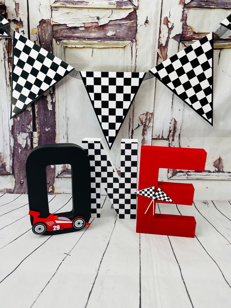 May include: Red, black and white "ONE" letters with a chequered pattern. The letter "O" has a red racing car with the number 29 on it. A chequered flag banner hangs above the letters.