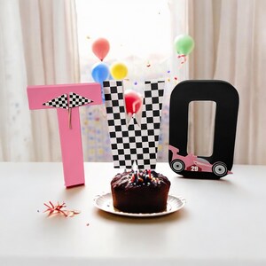 May include: Pink, black and white chequered, and black letter blocks spelling out the word "TWO" with a pink racing car in the letter "O". A chocolate cake with sprinkles sits in front of the blocks.