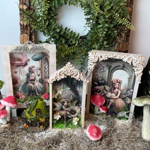Puede incluir: Una exhibición caprichosa con tres escenas de hadas enmarcadas en marcos ornamentados de color crema. Casitas de hadas en miniatura y setas con gorro rojo están dispersas entre el musgo. Una corona verde cuelga en el fondo, creando un tema de fantasía.