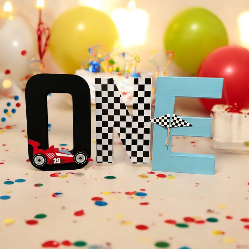 May include: Wooden letters spelling "ONE" in black, white and blue. The "O" has a red racing car with the number 29 on it. The "N" is black and white chequered. The "E" is light blue with a white chequered flag.