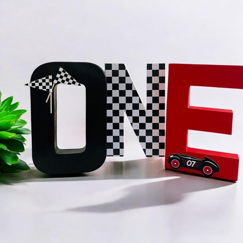 May include: Black, white and red wooden letters spelling "ONE" with a chequered pattern on the "N" and a red racing car with the number "07" on the "E".