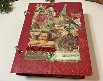 May include: Red journal with a textured cover and metal rings. The cover features a collage with a bird, angel, bells, and the phrase "all is bright." A red ribbon adds detail to the design. Christmas theme.