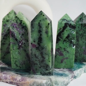 Könnte beinhalten: Fünf grüne, schwarze und violette Edelsteintürme auf einem violetten und grünen Steinsockel. Die Türme sind alle spitz und haben eine raue, natürliche Textur.