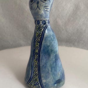 May include: A blue ceramic cat figurine with a decorative collar and floral accents. The cat has a stylized face with large eyes and whiskers. The figurine is approximately 8 inches tall.