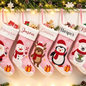 May include: Five pink Christmas stockings with white faux fur cuffs, each personalized with names Morgan, Jason, Emma, Harper, and Riley. The stockings feature embroidered holiday characters including Santa, a snowman, a reindeer, a penguin, and a polar bear.