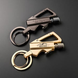 May include: Two metal keychains with integrated lighters. One is dark gray with the inscription "Hannah and 10.11.25". The other is gold with the inscription "BRIAN Best man". Both have a carabiner clip and a key ring.