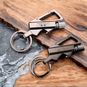 May include: Two personalized keychains with a lighter design. One is silver with "DOUGLAS Best man 10.11.2025" engraved. The other is dark gray with "Hannah and 10.11.2025" engraved. Both have a carabiner clip and a key ring.