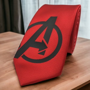Könnte beinhalten: Eine rote Krawatte mit einem schwarzen Avengers-Logo darauf.