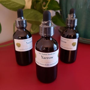 Puede incluir: Tres botellas de vidrio marrón oscuro con goteros, llenas de un líquido oscuro. Las botellas están etiquetadas con "The Herbal Touch LLC Yarrow" y enumeran los ingredientes: "Yarrow, Alcohol, and Distilled Water".