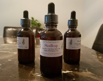 May include: Three brown glass bottles with dropper tops. The center bottle has a white label with the text "The Herbal Touch LLC Skullcap Directions: 2ml three times a day (Shake Well Before Use)"