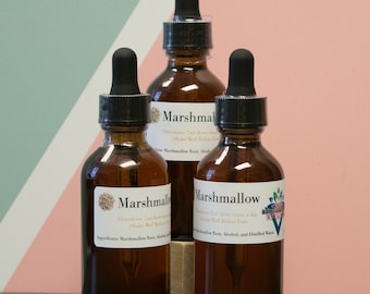 May include: Three amber glass bottles with dropper tops, labelled "Marshmallow" and containing a brown liquid. The bottles are on a green surface with a pink and green background.