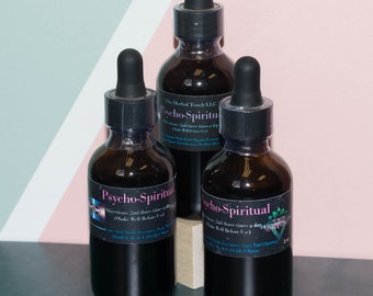 May include: Three brown glass bottles with black droppers, labeled "Psycho-Spiritual" in pink and white text. The bottles are filled with a dark liquid and are arranged on a green and pink surface.