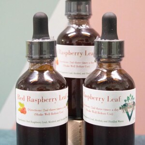 May include: Three glass bottles filled with a dark liquid, each with a black dropper and a white label. The labels read "Red Raspberry Leaf" and "Raspberry Leaf", with instructions for use. The bottles are arranged in front of a colorful background.