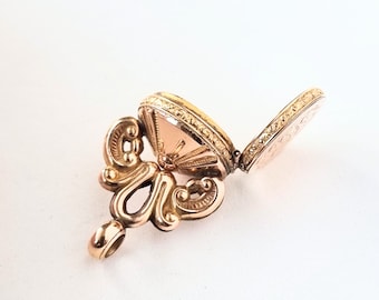 May include: A gold locket with an ornate design and a hinged lid. The locket is open, revealing a blank interior.