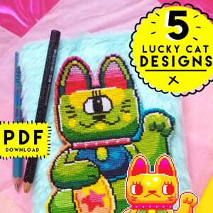 Puede incluir: Una libreta azul peluda con un diseño de gato de la suerte pixelado de colores. La libreta tiene una etiqueta amarilla que dice "PDF DOWNLOAD". Un círculo amarillo con un contorno blanco y texto negro dice "5 LUCKY CAT DESIGNS X".