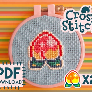 Op de afbeelding: Kruissteekpatroon van een rood en geel paddenstoelkarakter met groene laarzen. Het patroon zit in een roze borduurring en bevat de tekst "Cross Stitch" en "PDF Download x2".