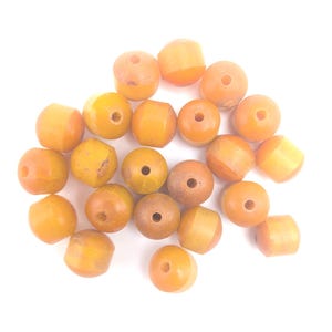 May include: A selection of amber-toned beads in various forms, including spherical and cylindrical. Each bead is pierced with a central hole, and the colours range from pale yellow to a deeper, brownish shade. Ideal for jewellery making.