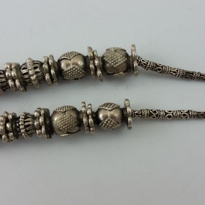 May include: A silver necklace with ornate beads and a clasp. The necklace is on a white background. The tag attached to the necklace reads "1/2man".