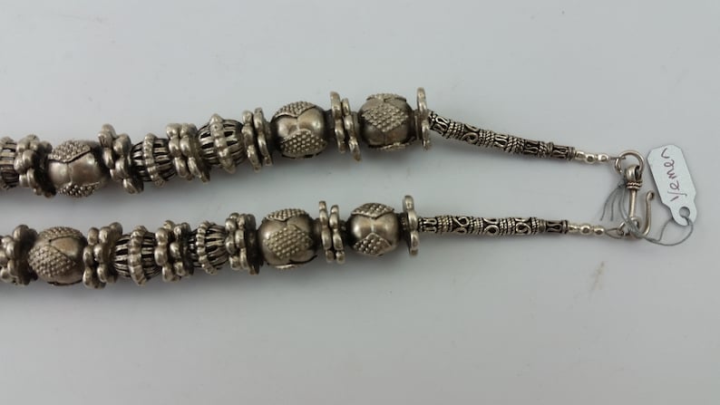 May include: A silver necklace with ornate beads and a clasp. The necklace is on a white background. The tag attached to the necklace reads "1/2man".