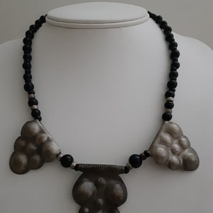 May include: A silver necklace with three pendant charms, each with a textured, bubble-like design. The necklace is strung with black beads.