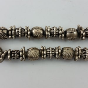 May include: A silver necklace featuring a decorative pendant and a chain of intricately designed beads.
