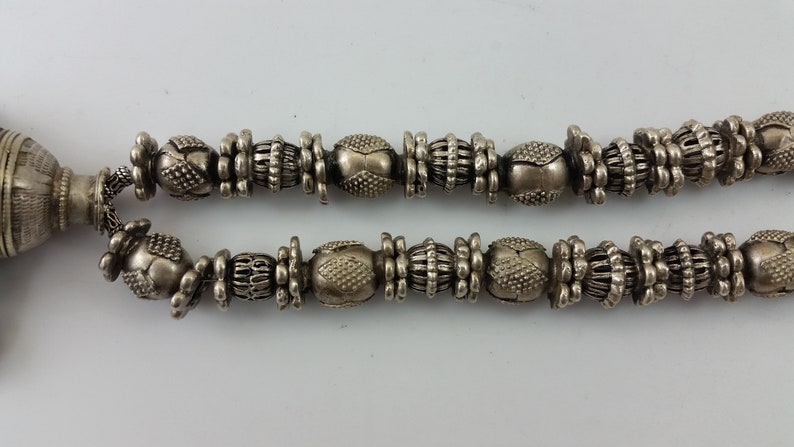 May include: A silver necklace featuring a decorative pendant and a chain of intricately designed beads.