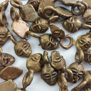 May include: A group of 20 small, gold-colored metal charms with a face design. Each charm has a small loop at the top for attaching to a necklace or bracelet.
