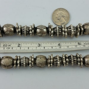 May include: A silver necklace with large, ornate beads. The necklace is approximately 15 inches long and is made of metal beads with a textured surface. The beads are arranged in a repeating pattern of three beads.