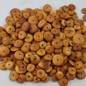 May include: A pile of round, wooden beads in various sizes and shades of tan and brown. Each bead has a central hole. The beads are scattered on a white surface, suggesting a craft or jewelry-making theme.