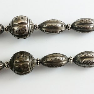 May include: A silver necklace with a hook clasp and oval-shaped beads with intricate designs. The beads are all the same size and are evenly spaced.