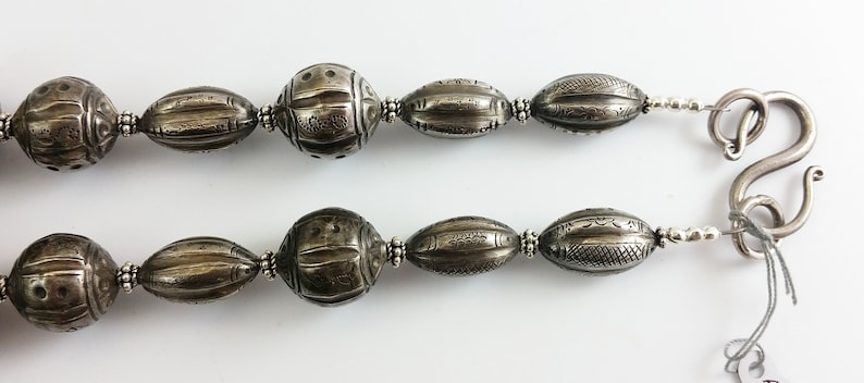 May include: A silver necklace with a hook clasp and oval-shaped beads with intricate designs. The beads are all the same size and are evenly spaced.