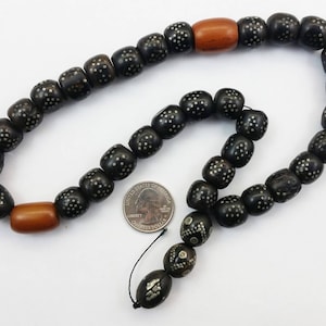 Pu&ograve; includere: Una collana di perline nere e argentate con due perline di legno marrone. La collana &egrave; composta da perline rotonde con un motivo di piccoli punti argentati.